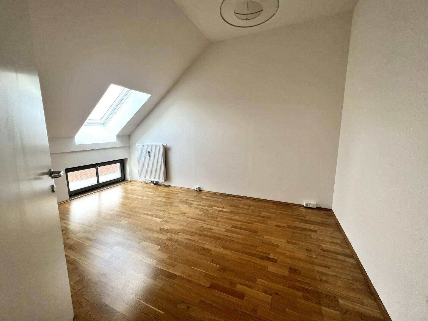 Ruhiges Schlafzimmer im Dachgeschoss mit Parkettboden, Dachfenster und Heizkörper.