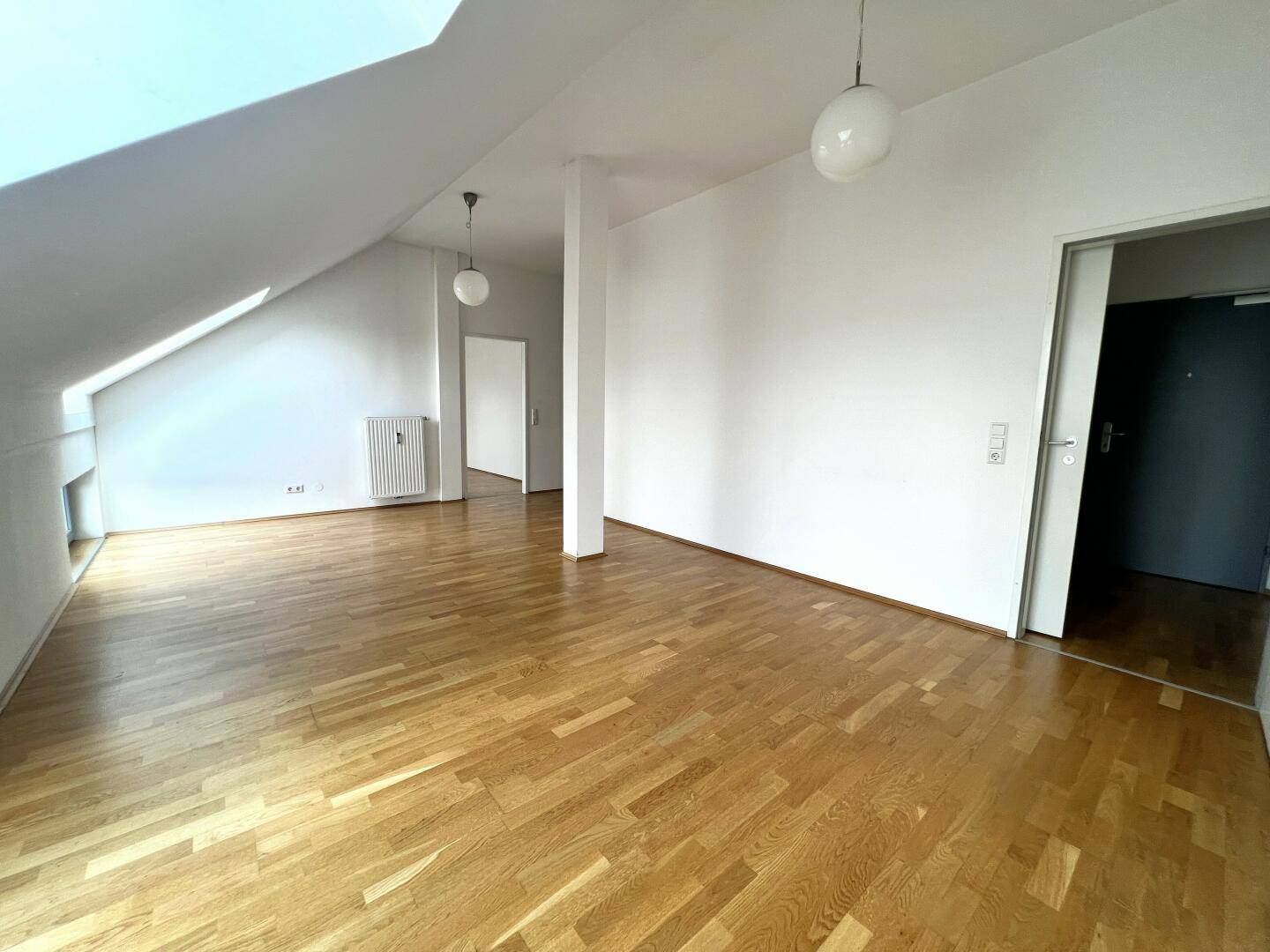 Heller Dachgeschossraum mit Parkettboden, weißen Wänden und Zugang zu weiteren Zimmern.