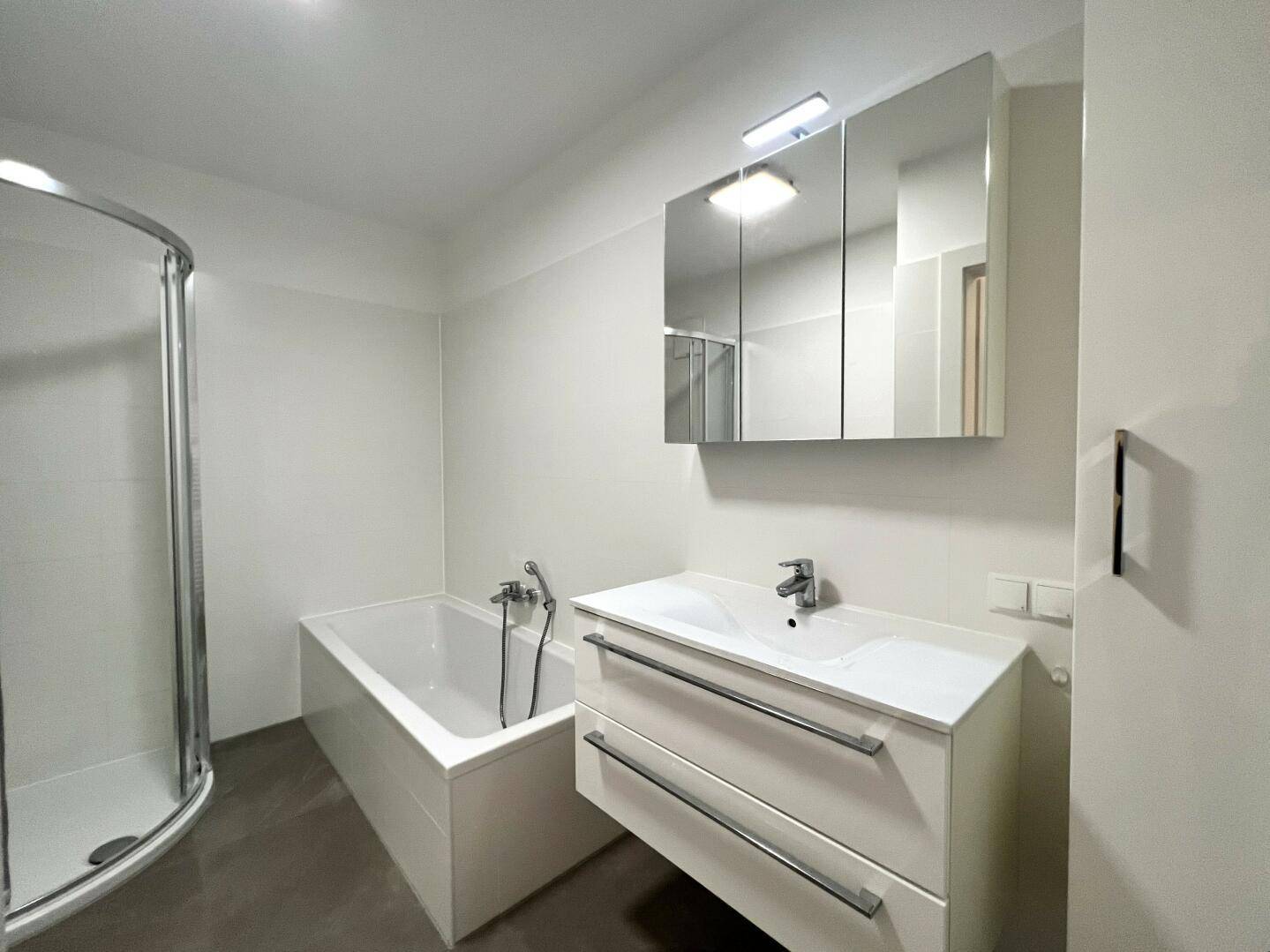 Helles Badezimmer mit Badewanne, Dusche und modernem Waschtisch mit Spiegelschrank.