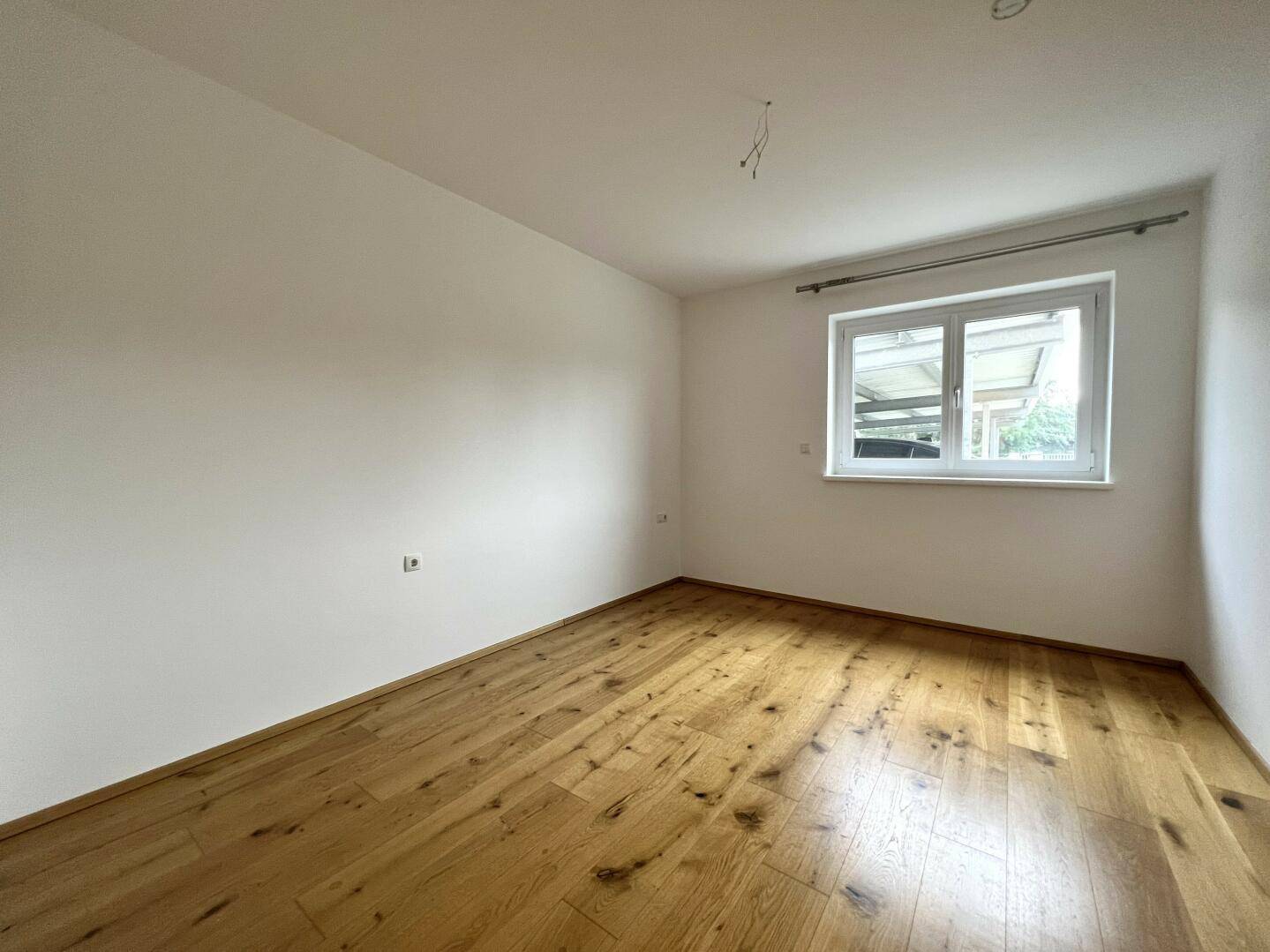 Helles Schlafzimmer mit Holzboden und großem Fenster, bereit zur individuellen Gestaltung.