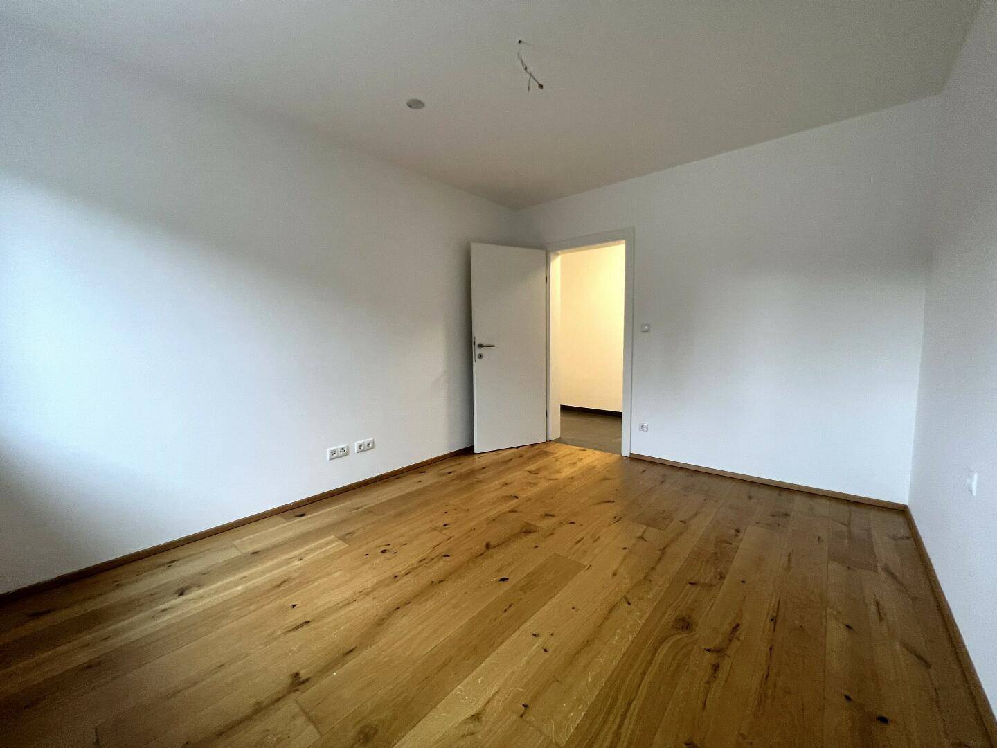 Leeres Schlafzimmer mit Holzboden und weiß gestrichenen Wänden, ideal für neue Einrichtung.