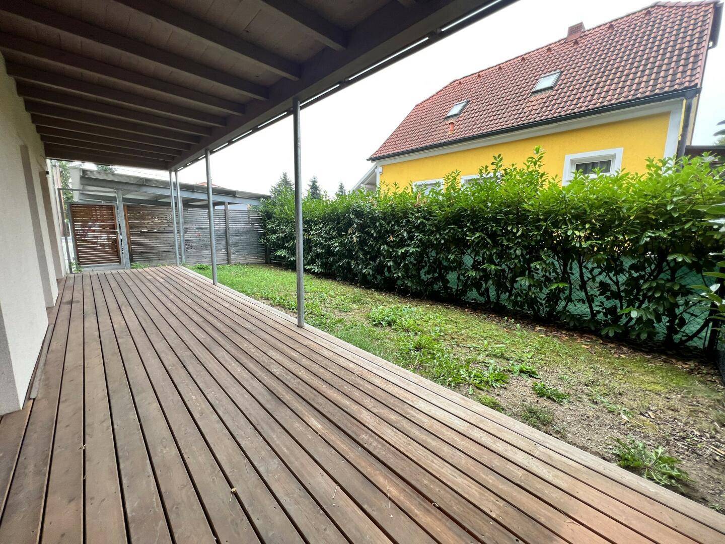 Geräumige Holzterrasse mit Gartenbereich und Hecke als Sichtschutz.