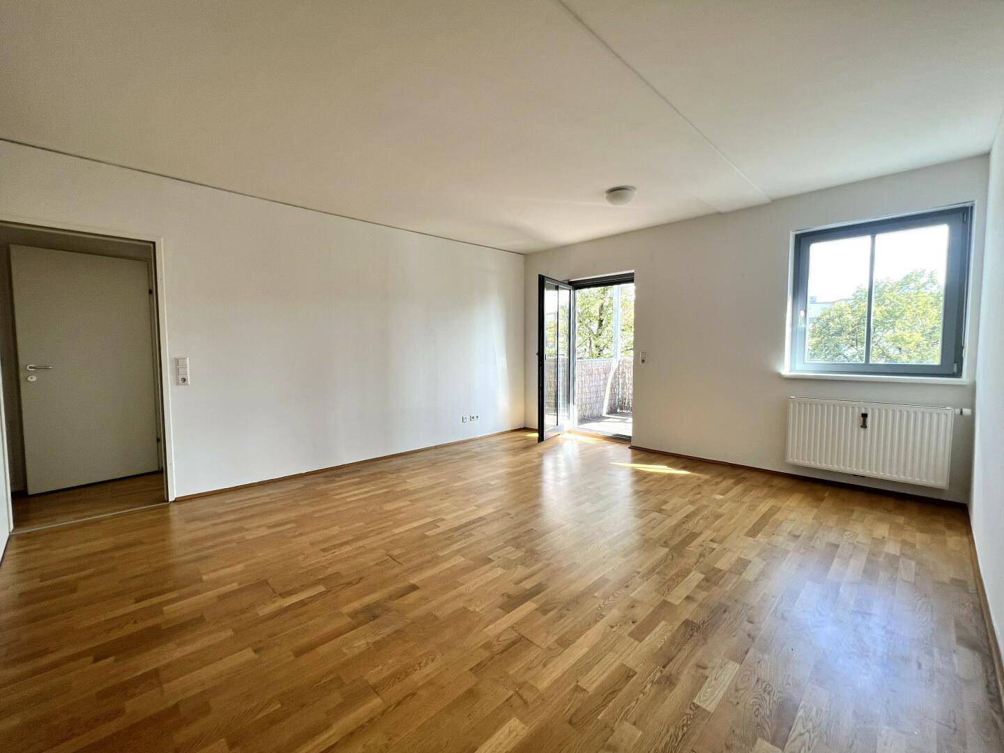 Geräumiges Wohnzimmer mit Parkettboden, viel Tageslicht und Zugang zum Balkon.