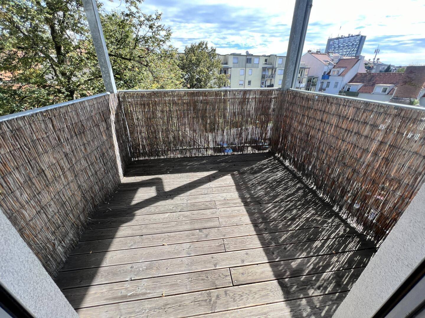 Gemütlicher Balkon mit Holzboden und Sichtschutz, bietet einen Blick auf die Stadt.