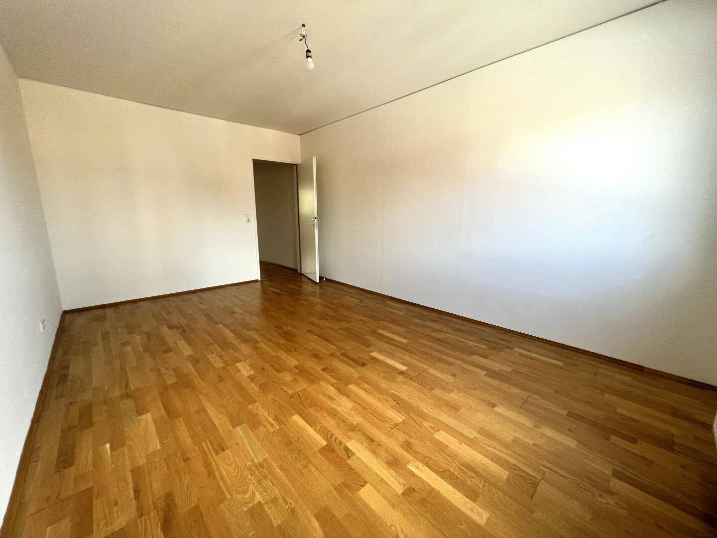 Helles Zimmer mit Parkettboden und Zugang zu einem weiteren Raum, vielseitig nutzbar.