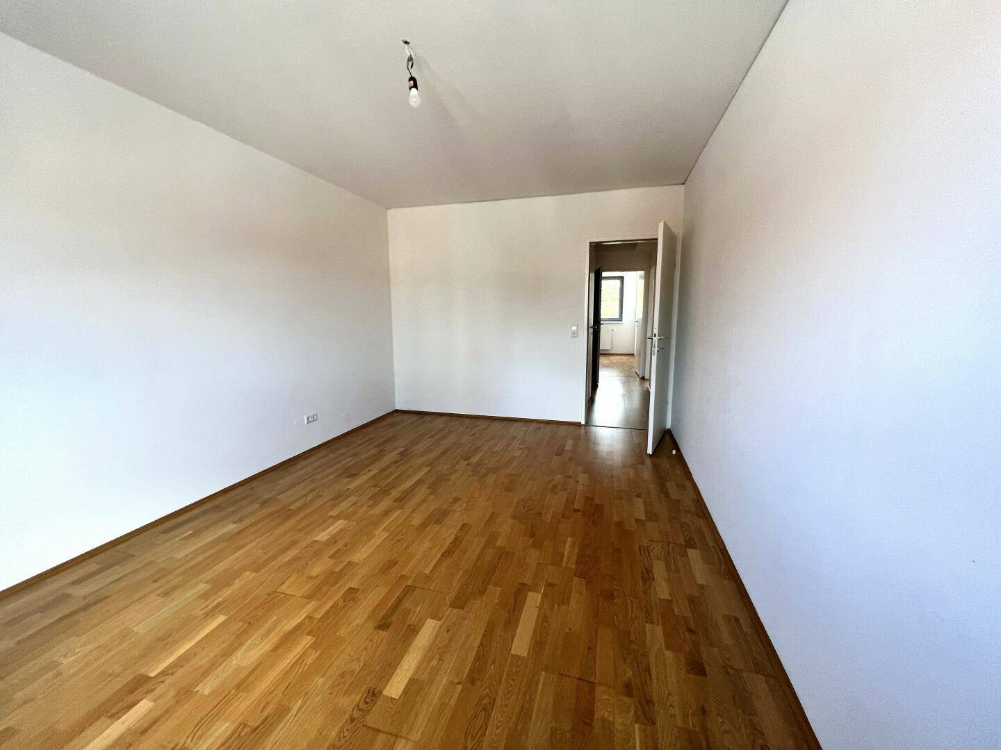 Leeres Zimmer mit Parkettboden und offener Tür, bietet flexible Gestaltungsmöglichkeiten.