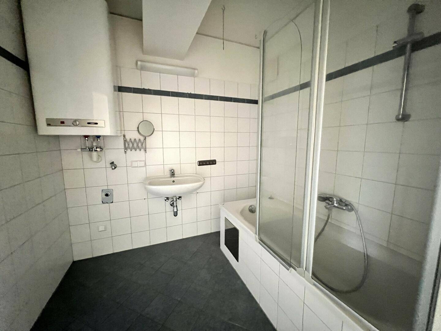 Badezimmer mit Badewanne, Duschabtrennung, Waschbecken und Wandfliesen in Weiß und Dunkelblau.