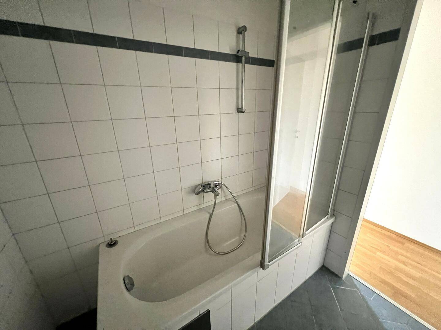 Badewanne mit Duschabtrennung und Armatur in einem gefliesten Badezimmer.
