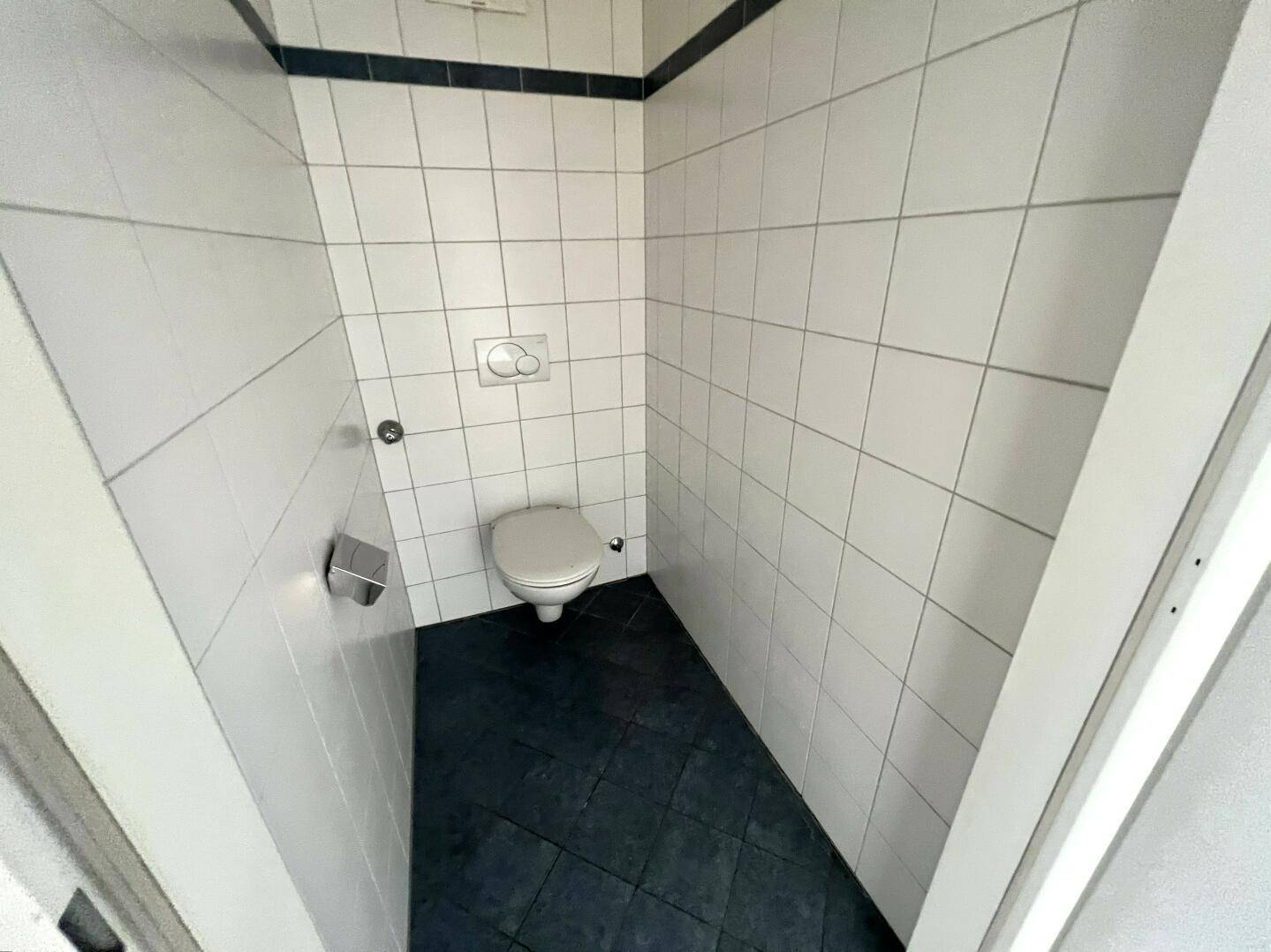 Separates WC mit wandhängender Toilette und Fliesen in Weiß und Dunkelblau.