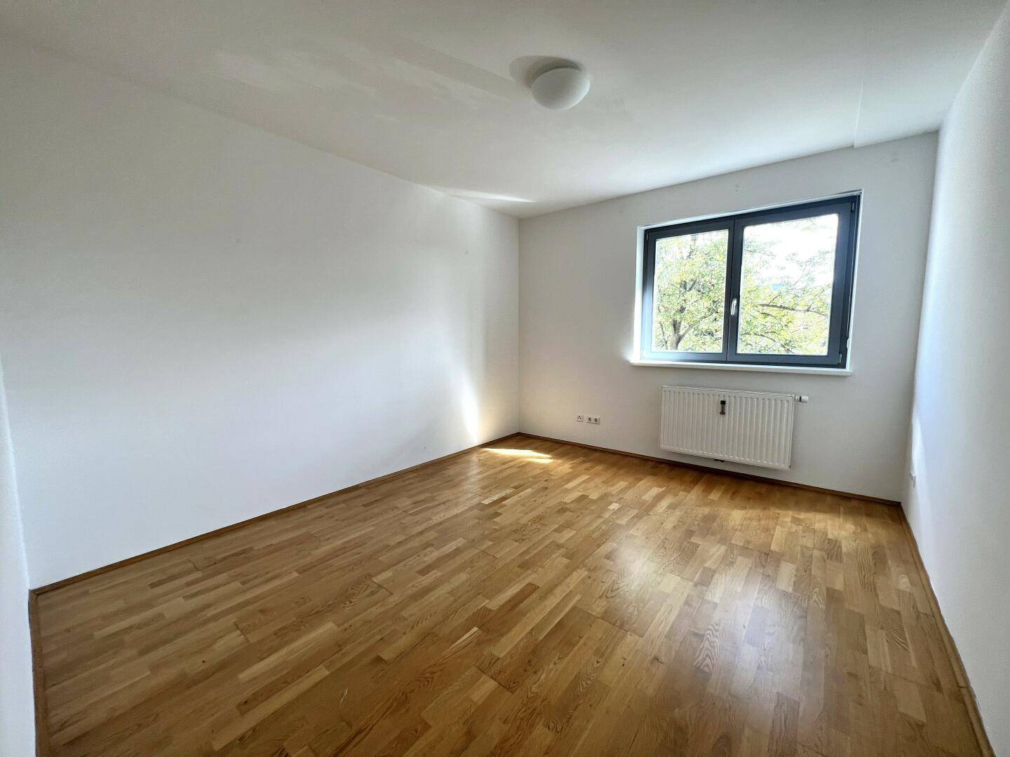 Helles, leeres Zimmer mit Parkettboden und Fenster, ideal als Schlaf- oder Kinderzimmer.