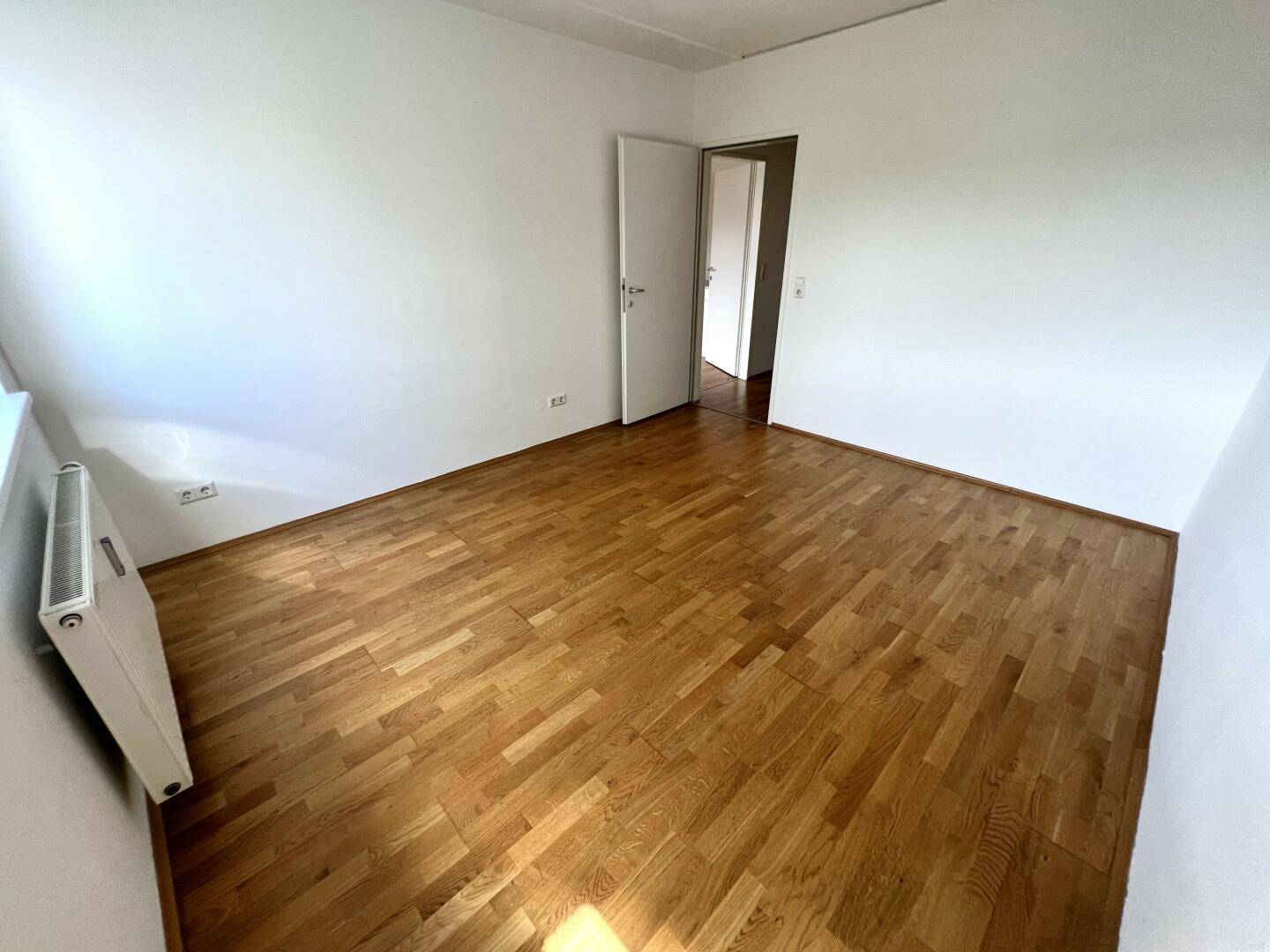Geräumiges, leeres Zimmer mit Parkettboden und offener Tür, bietet vielseitige Nutzungsmöglichkeiten.