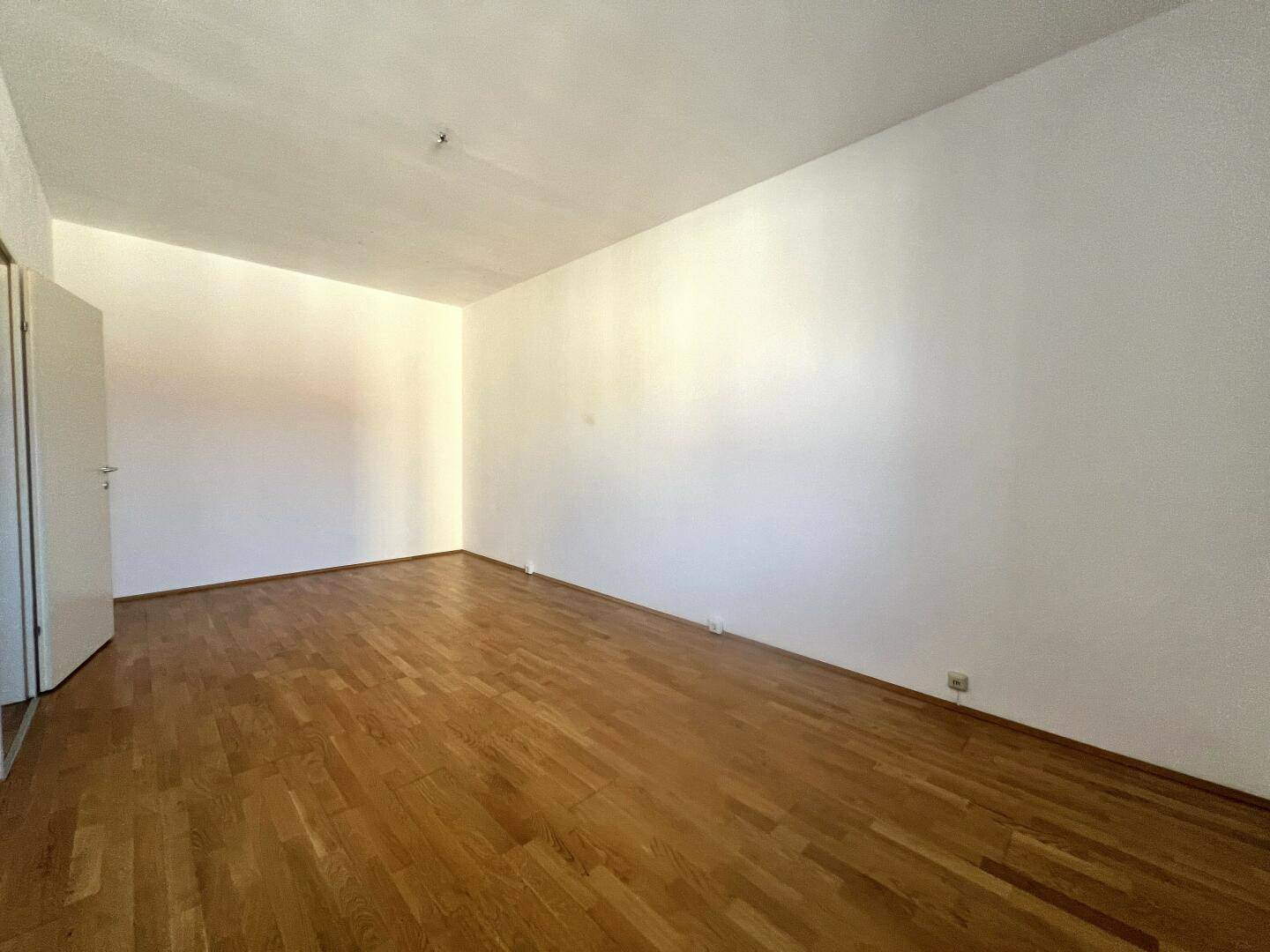 Heller, leerer Raum mit Parkettboden und weißen Wänden, ideal für vielfältige Nutzung.