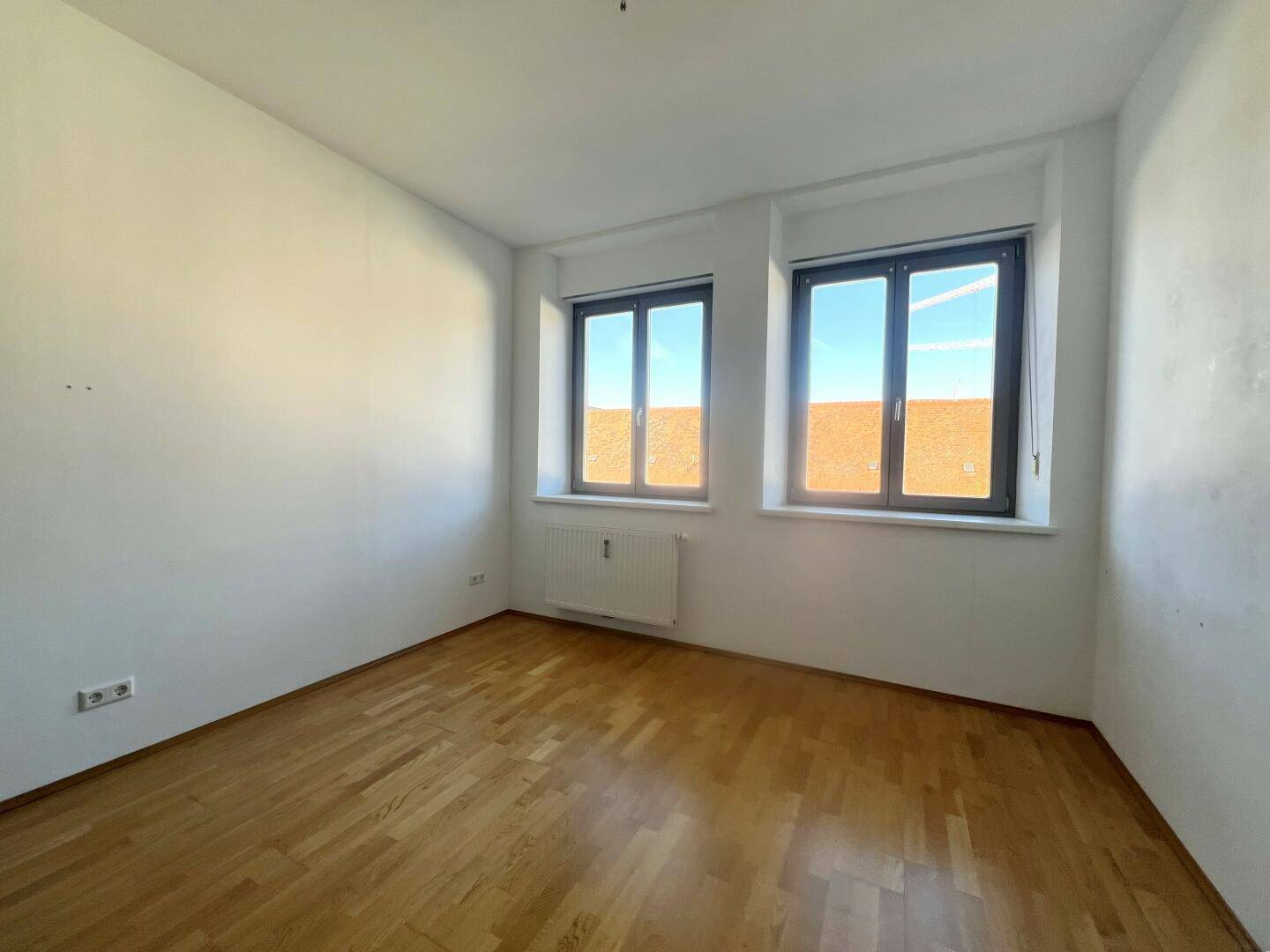 Lichtdurchfluteter Raum mit Parkettboden und zwei Fenstern, bietet viel Tageslicht.