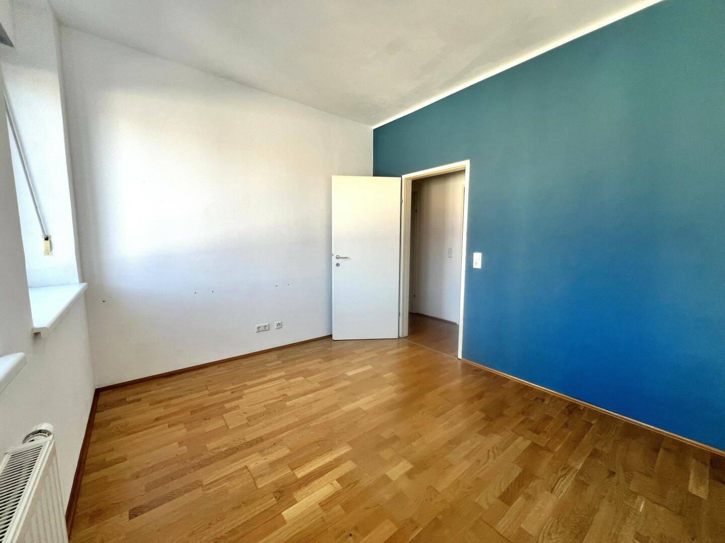 Leerer Raum mit Parkettboden und einer blauen Akzentwand, bereit zur Einrichtung.