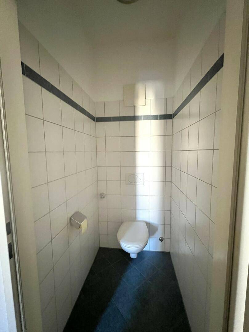 Kleines Gäste-WC mit weißen Fliesen, dunklem Boden und wandhängendem WC.