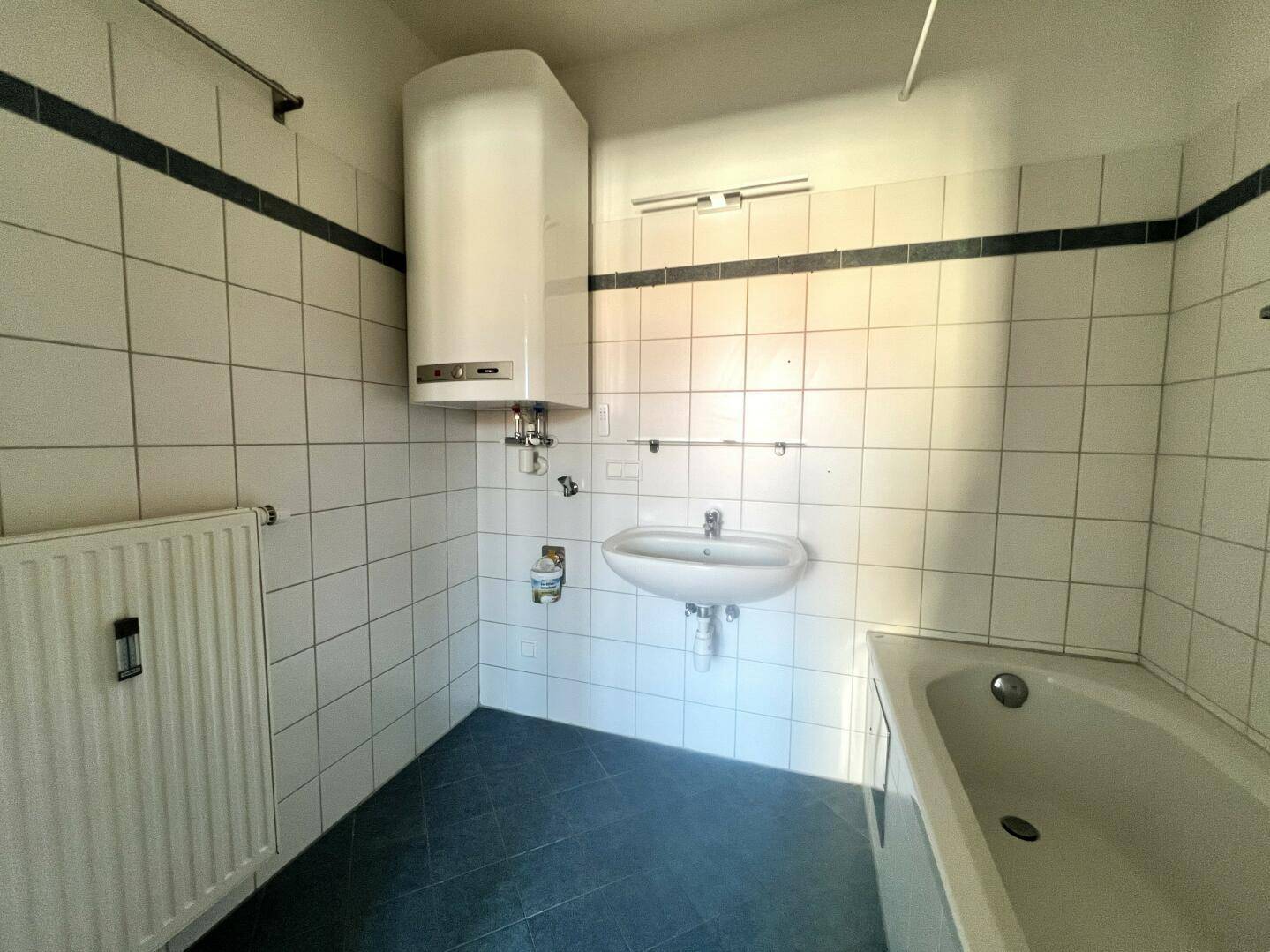 Badezimmer mit Badewanne, Waschbecken, Boiler und weißen Wandfliesen, funktional ausgestattet.
