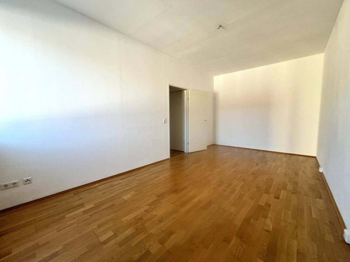 Leerer Raum mit Parkettboden und weißen Wänden, bereit zur individuellen Gestaltung.