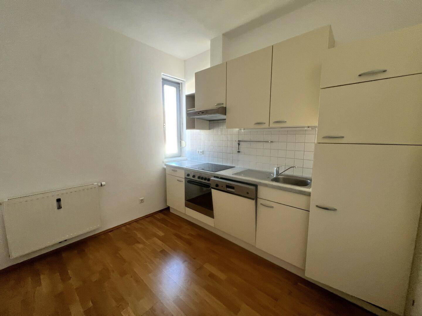 Helle Einbauküche mit Fenster, ausgestattet mit Herd, Spülbecken und Oberschränken.