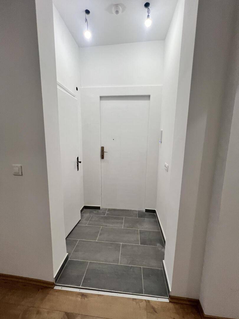 Eingangsbereich mit grauen Bodenfliesen und weißer Tür, die in die Wohnung führt.