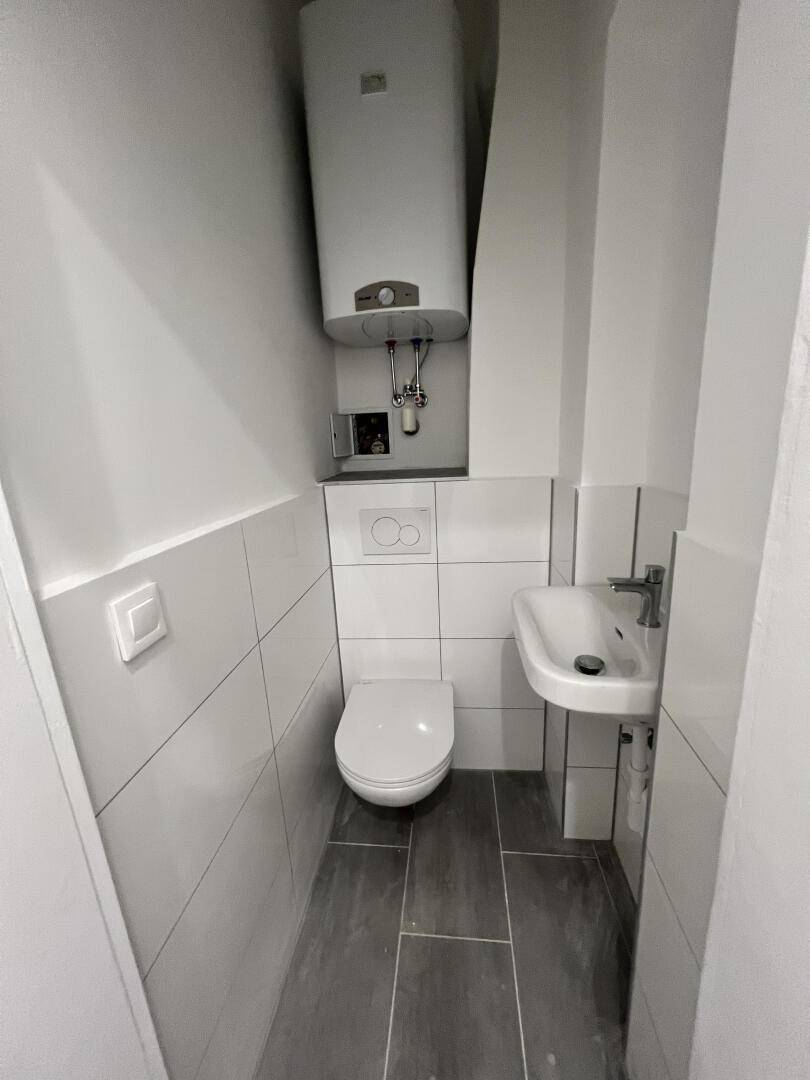 Kleines Gäste-WC mit wandhängender Toilette, Waschbecken und Warmwasserboiler.