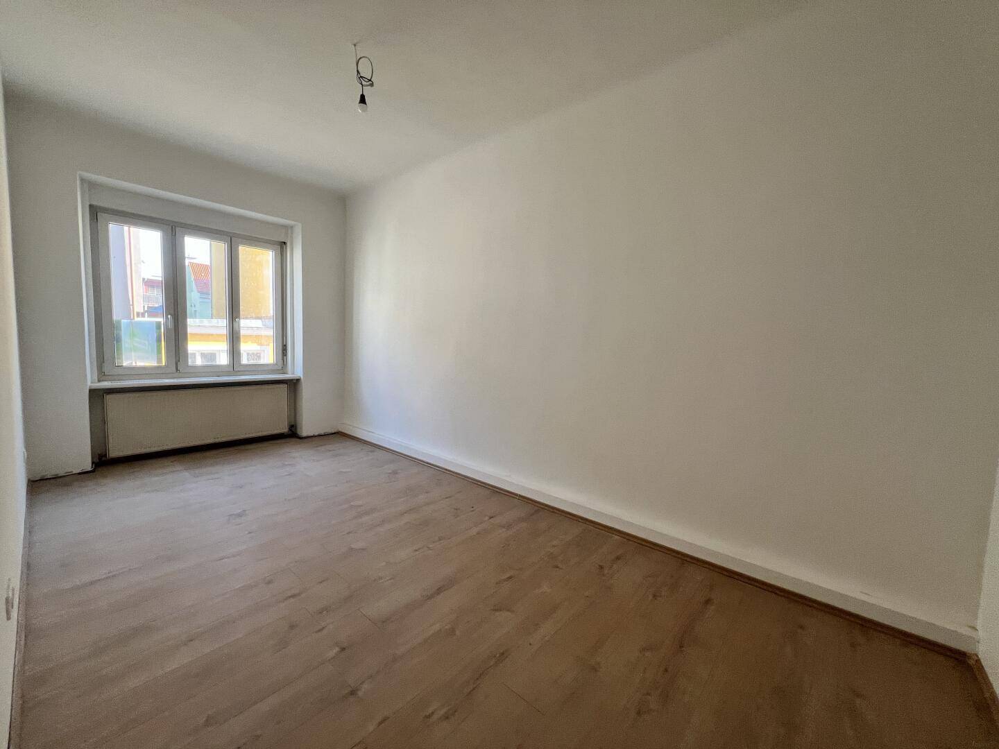 Großes, helles Zimmer mit Laminatboden und Fenster, das viel Tageslicht bietet.