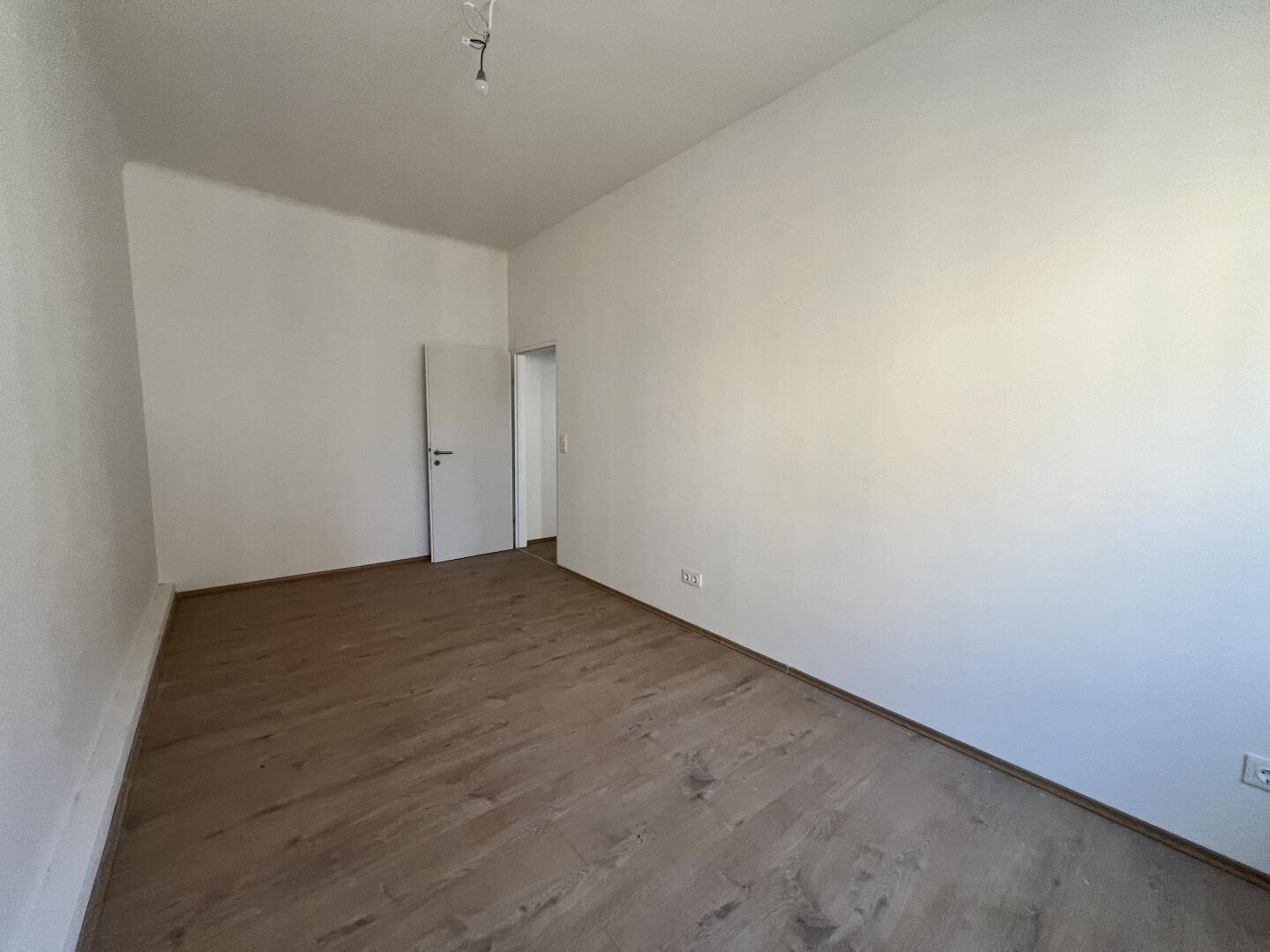 Geräumiges Zimmer mit Laminatboden und weiß gestrichenen Wänden, bereit zur Einrichtung.