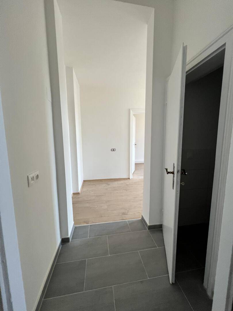 Heller Flur mit modernen grauen Fliesen, der zu weiteren Räumen mit Laminatboden führt.