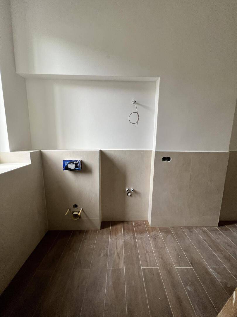 Unfertiges Badezimmer mit vorbereiteten Anschlüssen für Waschtisch und Toilette.