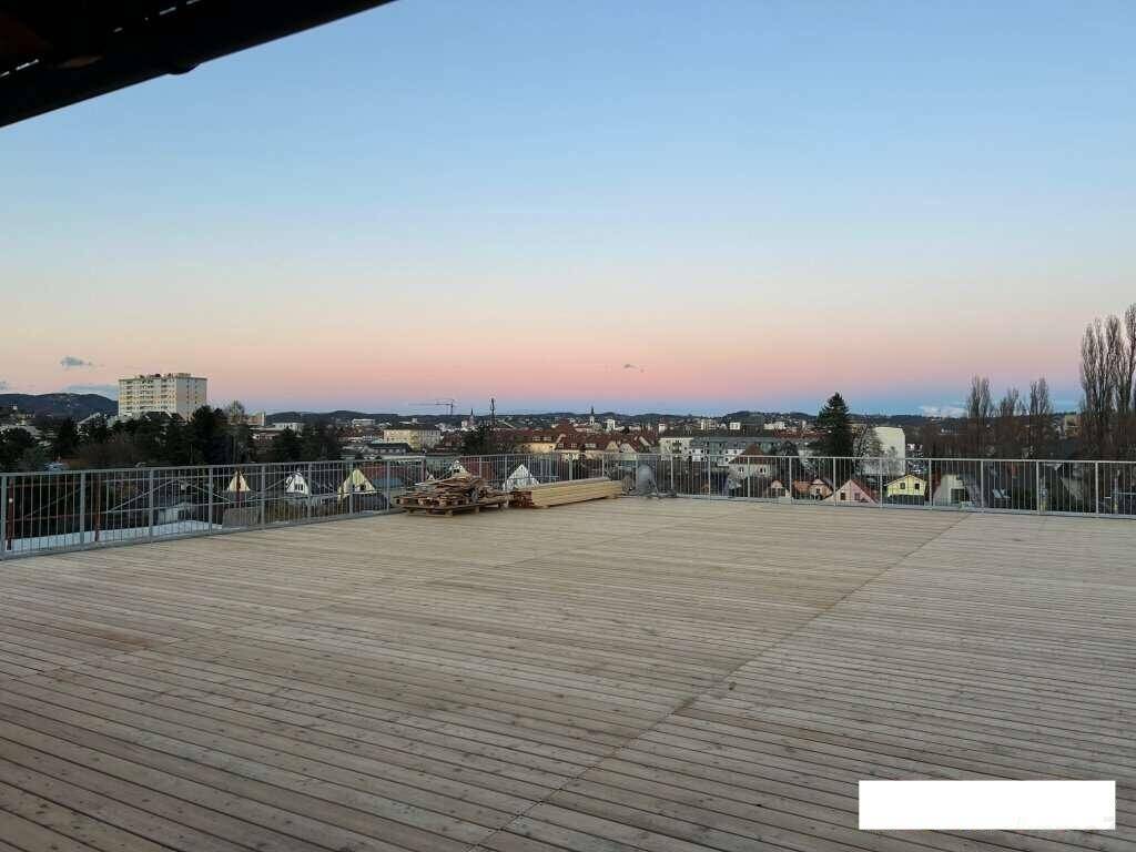 Weitläufige Holzterrasse mit Stadtblick bei Sonnenuntergang, ideal für Abendstunden.