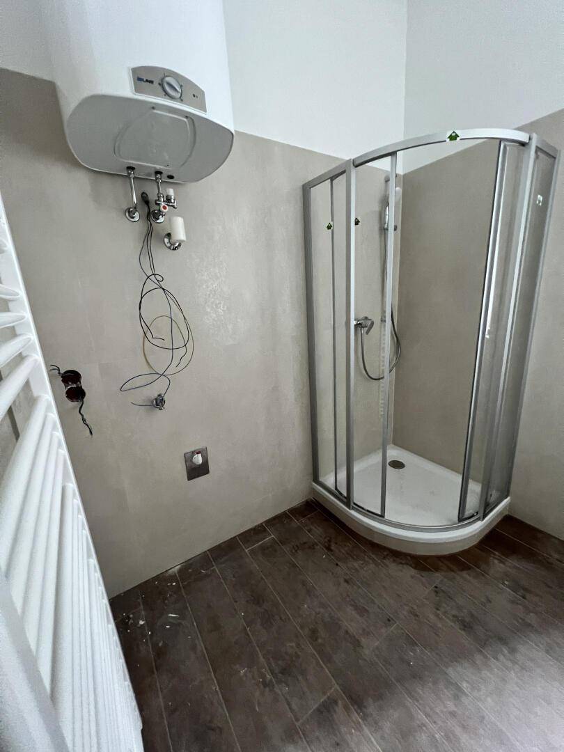 Unfertiges Badezimmer mit Eckduschkabine und Warmwasserboiler, bereit zur Fertigstellung.