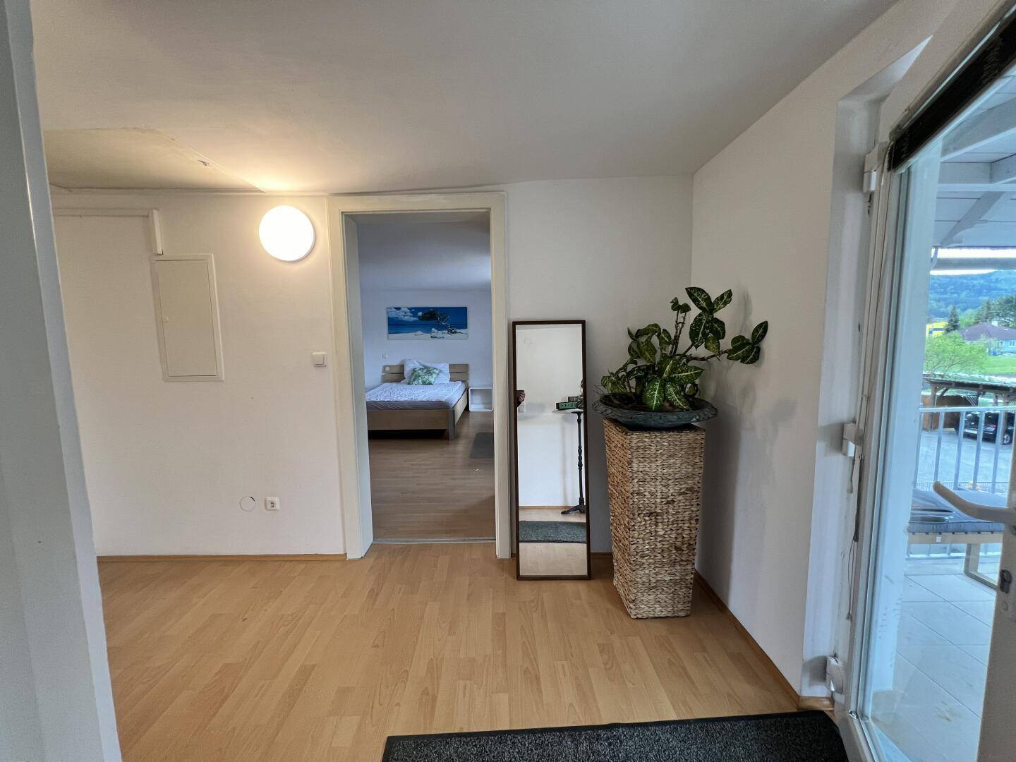 Heller Flur mit Holzboden, Spiegel und Zugang zum Schlafzimmer und zum überdachten Balkon.