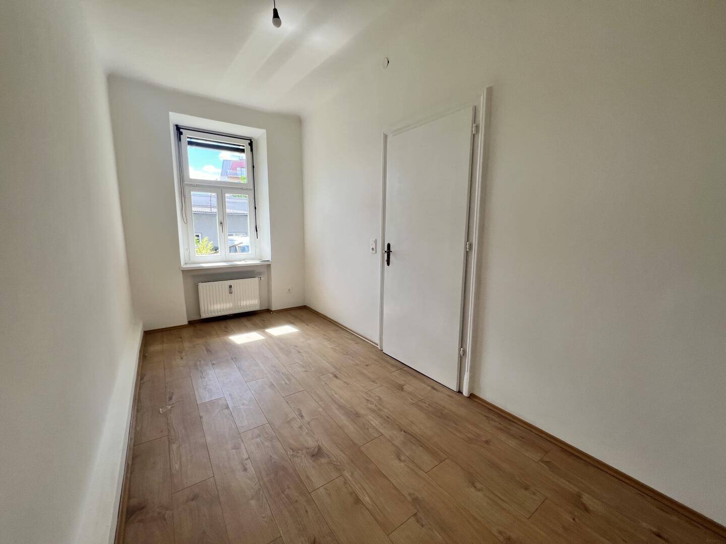 Helles Zimmer mit Laminatboden und Fenster, das viel Tageslicht hereinlässt.