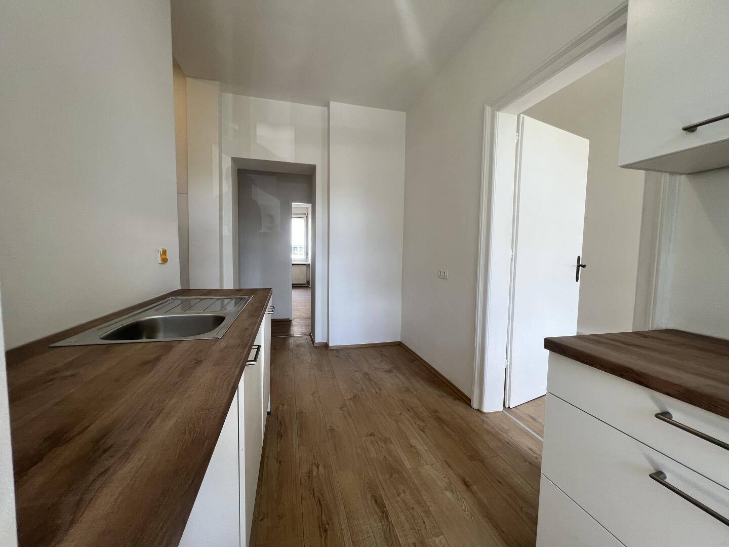 Küche mit Holzarbeitsplatte und Spüle, Blick in den Flur und weitere Zimmer.