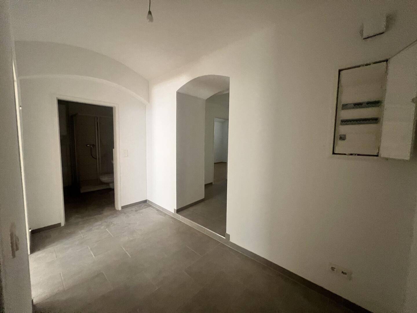 Heller Flur mit dunklen Fliesen und Zugang zu weiteren Räumen, inklusive Badezimmer.