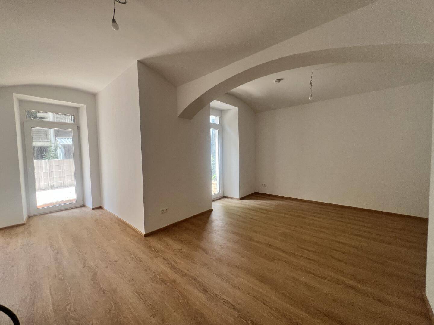 Geräumiges Wohnzimmer mit Holzboden, hohen Decken und Zugang zu einem Außenbereich.