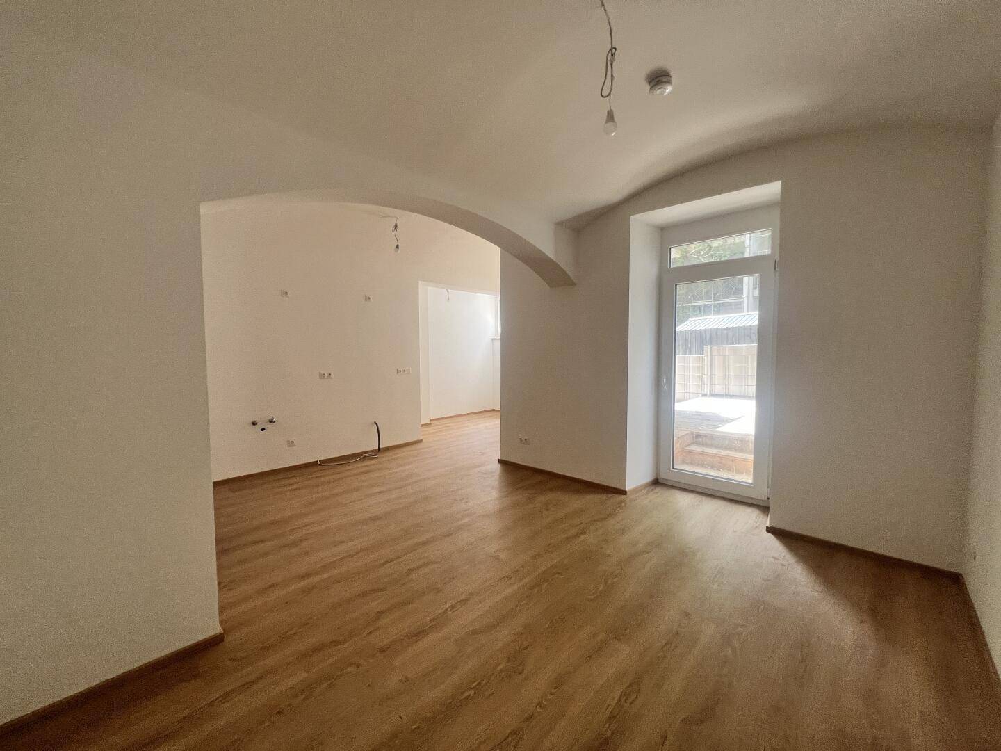 Lichtdurchfluteter Raum mit Laminatboden und Zugang zu einem Außenbereich, mit gewölbter Decke.