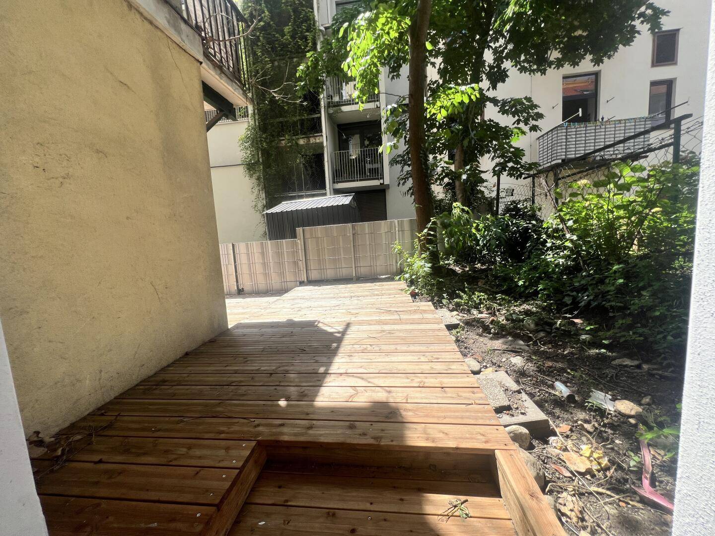 Holzterrasse im Hinterhof mit angrenzendem Grünbereich und Blick auf das Gebäude.