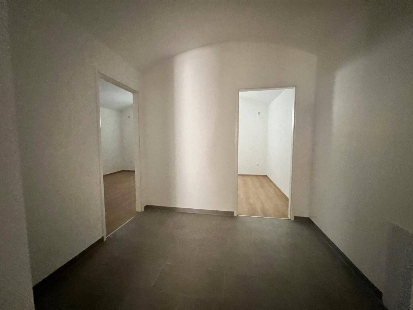 Heller Flur mit dunklen Fliesen und Zugang zu zwei weiteren, leeren Räumen.
