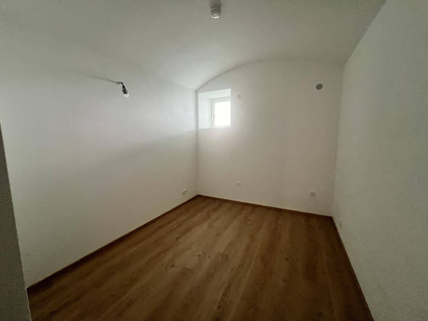 Kleines, helles Zimmer mit Laminatboden und Fenster, ideal als Schlaf- oder Arbeitszimmer.