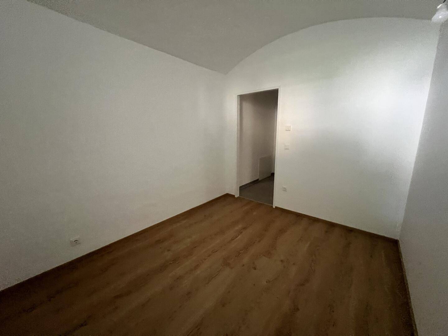 Leeres Zimmer mit Laminatboden und gewölbter Decke, bereit zur individuellen Gestaltung.