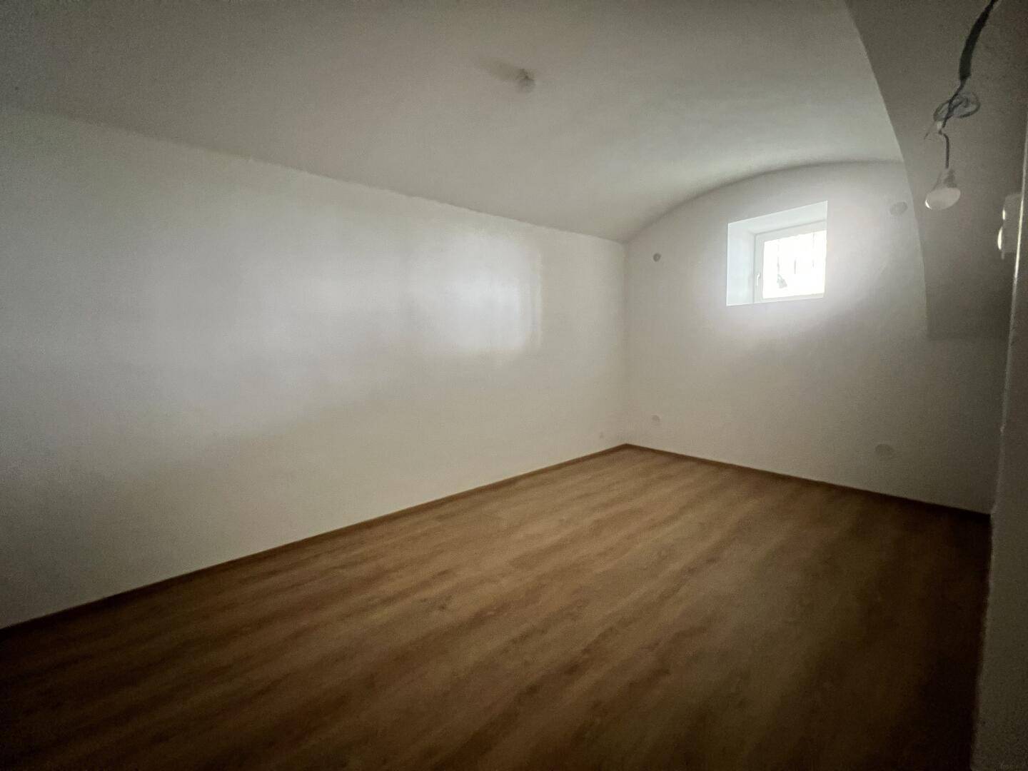 Helles Zimmer mit Laminatboden und kleinem Fenster, bietet vielseitige Nutzungsmöglichkeiten.