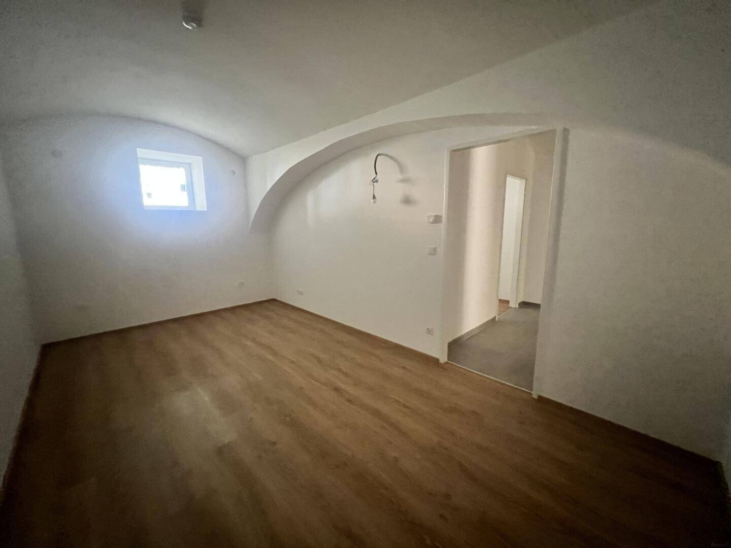 Lichtdurchflutetes Zimmer mit Laminatboden und gewölbter Decke, bietet eine angenehme Atmosphäre.