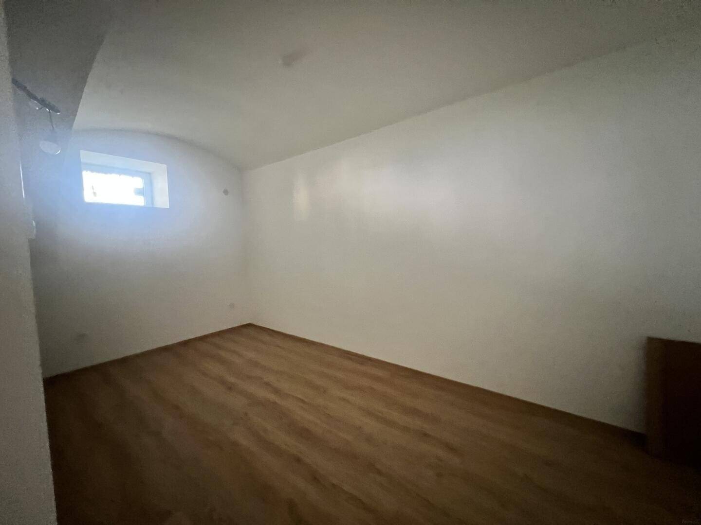 Kellerraum mit kleinem Fenster und Laminatboden, nutzbar als Abstell- oder Hobbyraum.