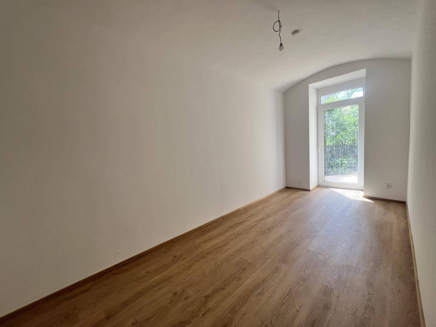 Heller Raum mit großem Fenster und Laminatboden, bietet Zugang zum Außenbereich.