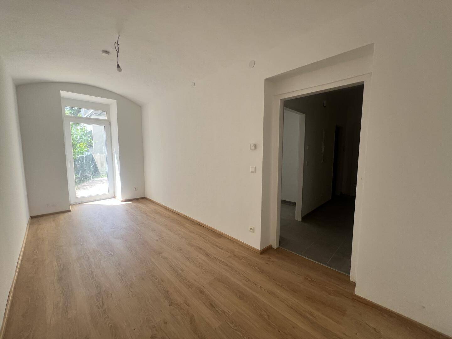 Geräumiges Wohnzimmer mit Laminatboden und Zugang zu einem weiteren Raum.