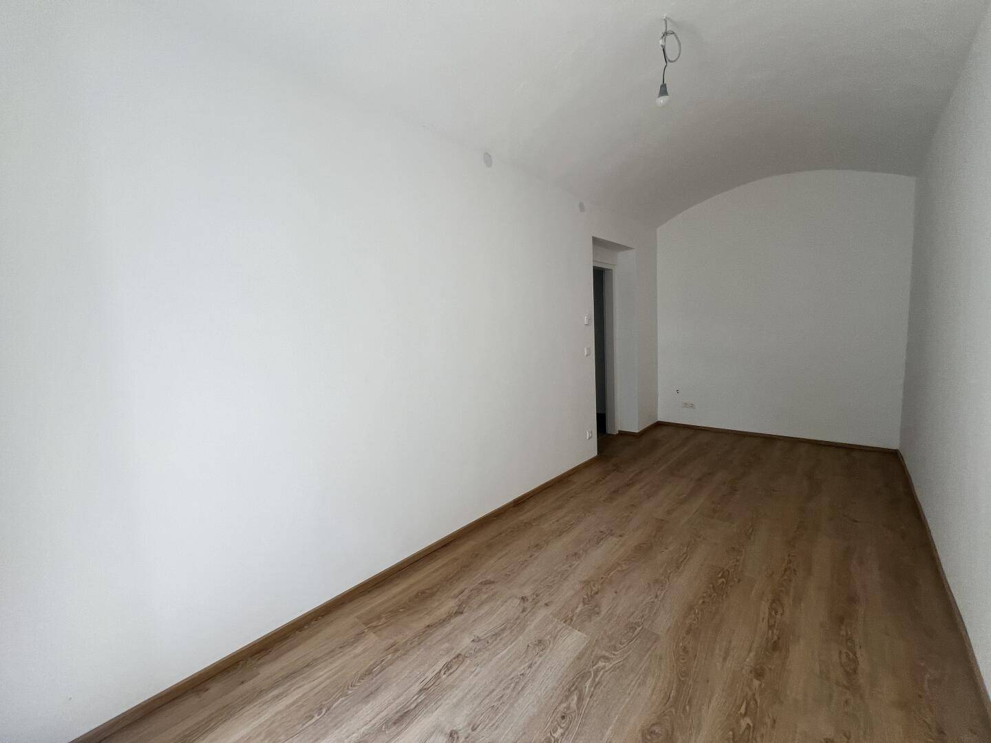 Leerer Raum mit gewölbter Decke und Laminatboden, ideal für individuelle Einrichtung.