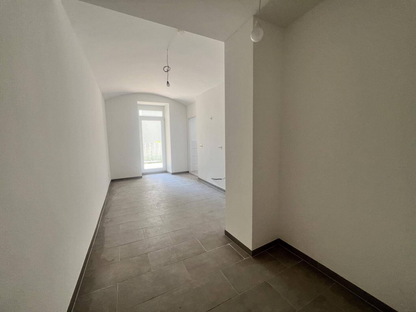 Heller Flur mit modernen grauen Fliesen und Zugang zum Außenbereich.
