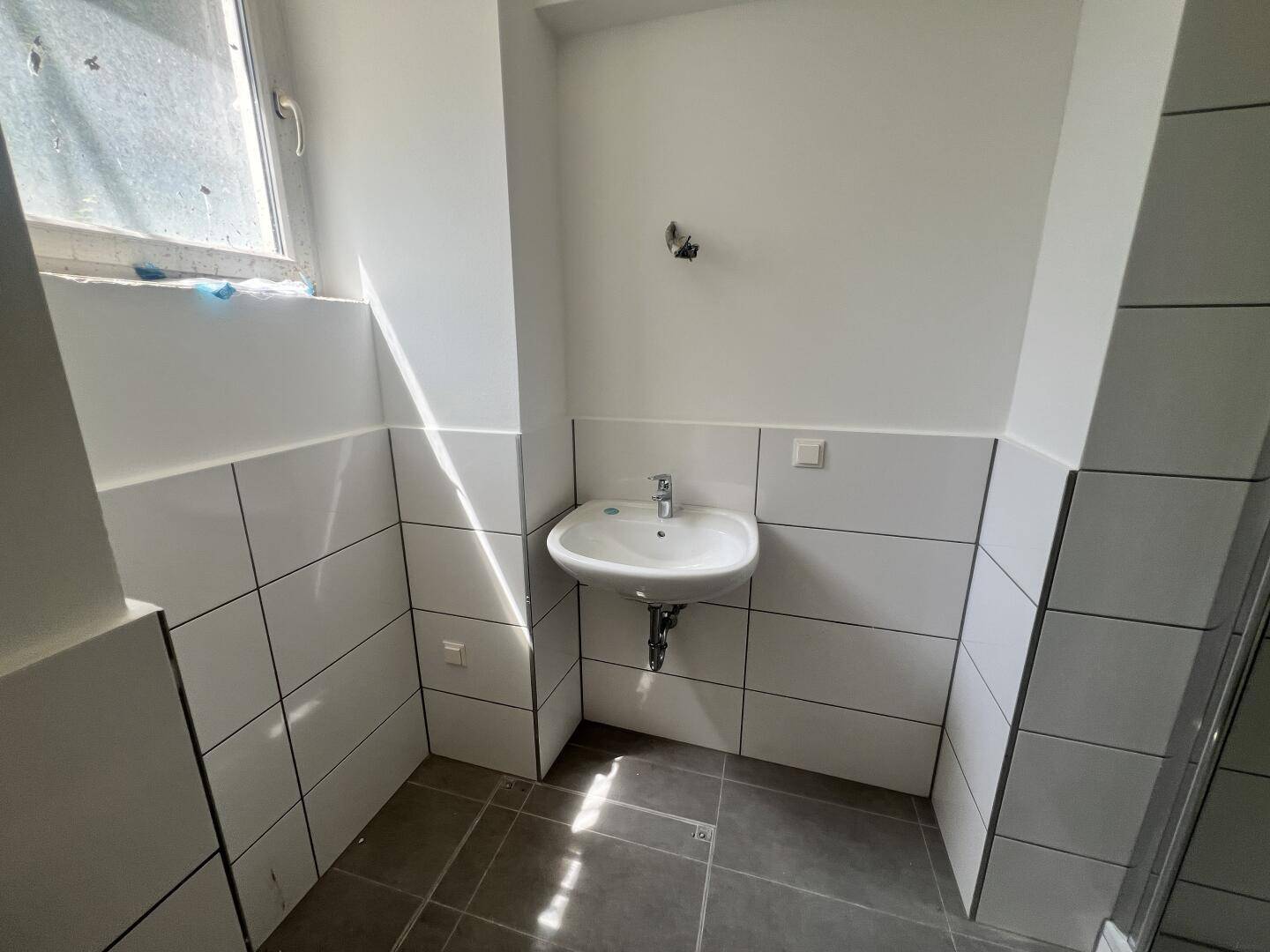 Helles Badezimmer mit Waschbecken, Fenster und modernen Fliesen.