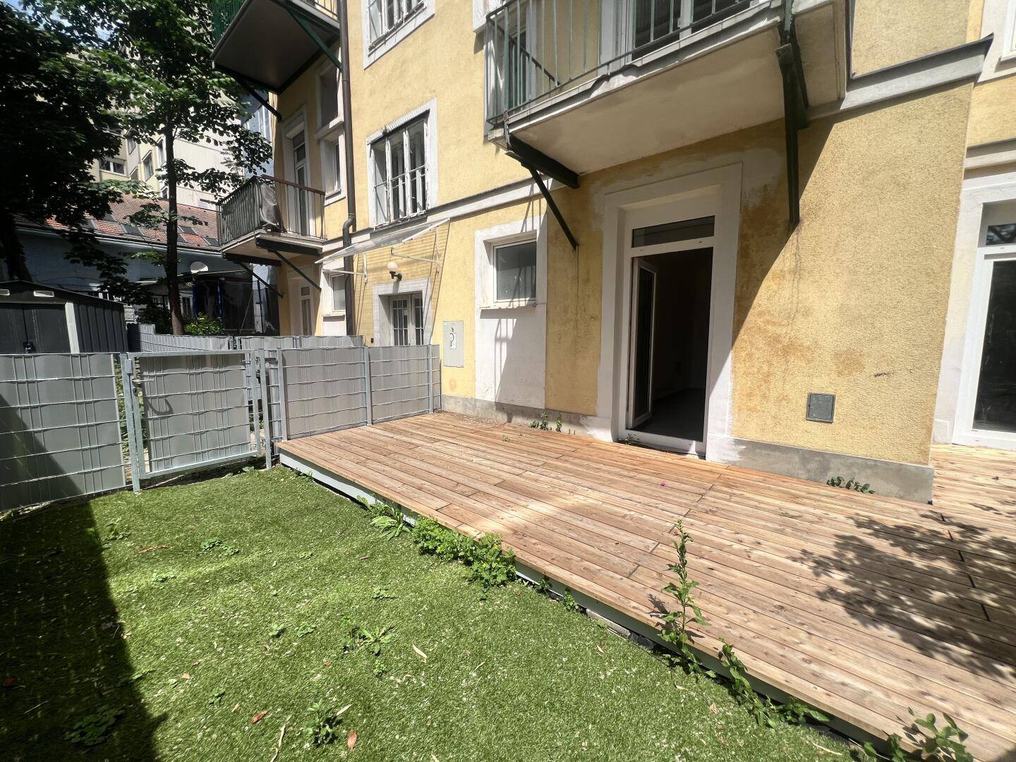 Gepflegte Holzterrasse mit Rasenfläche und direktem Zugang zum Gebäude.