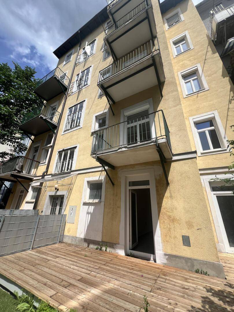 Fassade eines Mehrfamilienhauses mit Balkonen und einer Erdgeschossterrasse.